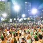 Público lota área de shows durante evento de Carnaval em Fortaleza, com palco iluminado, músicos e foliões reunidos em espaço urbano à noite.