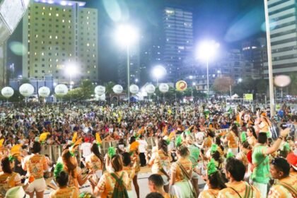 Público lota área de shows durante evento de Carnaval em Fortaleza, com palco iluminado, músicos e foliões reunidos em espaço urbano à noite.