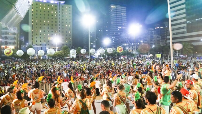 Público lota área de shows durante evento de Carnaval em Fortaleza, com palco iluminado, músicos e foliões reunidos em espaço urbano à noite.