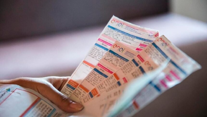 Mão segura várias contas de energia da Enel, ilustrando o novo desconto concedido a famílias inscritas no CadÚnico.