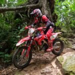 Motociclista de rally desce trecho rochoso em trilha cercada por vegetação, durante competição off-road do Cerapió.