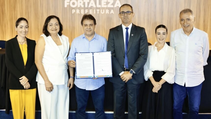 Autoridades municipais e representantes do Governo Federal posam durante a assinatura do termo de adesão de Fortaleza ao Programa de Privacidade e Segurança da Informação, com o prefeito segurando o documento oficial no auditório da Prefeitura.