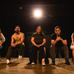 Grupo Bagaceira sentado no palco, sob iluminação cênica, durante ensaio do espetáculo “Inacabado” no teatro.