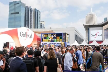 Multidão de visitantes circula entre estandes da feira Gulfood, em Dubai, com pavilhões identificados pelo nome do evento e prédios modernos ao fundo.