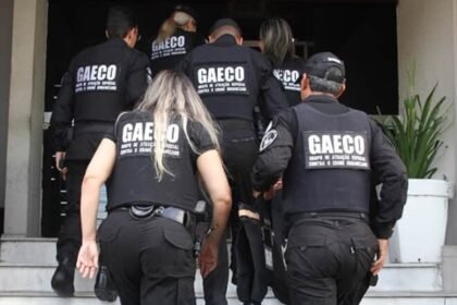 Agentes do Gaeco sobem escadaria de prédio durante operação, vestindo coletes pretos com identificação do grupo de combate às organizações criminosas.