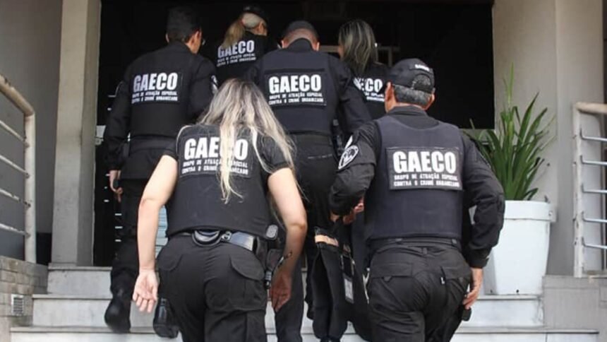 Agentes do Gaeco sobem escadaria de prédio durante operação, vestindo coletes pretos com identificação do grupo de combate às organizações criminosas.