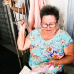 Mulher sentada borda manualmente um tecido em bastidor, dentro de casa, em Aracati, durante ação da CeArt que amplia o acesso à Identidade Artesanal.