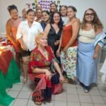 Grupo de mulheres empreendedoras reunidas em sala comunitária, ao lado de mesas com produtos artesanais e alimentos, durante preparação para a Feira Negócio de Bairro no Conjunto Palmeiras.