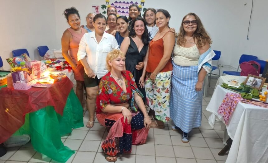 Grupo de mulheres empreendedoras reunidas em sala comunitária, ao lado de mesas com produtos artesanais e alimentos, durante preparação para a Feira Negócio de Bairro no Conjunto Palmeiras.