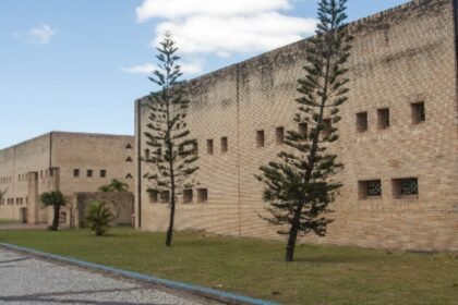 Fachada da sede da Secretaria de Cultura e Turismo de Eusébio, prédio em tijolos aparentes com área ajardinada e árvores ao longo da calçada.