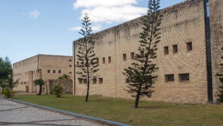 Fachada da sede da Secretaria de Cultura e Turismo de Eusébio, prédio em tijolos aparentes com área ajardinada e árvores ao longo da calçada.