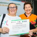 Mulher sorri segurando certificado de conclusão de curso profissionalizante ao lado de representante do Governo do Ceará, em cerimônia de qualificação profissional.