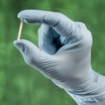 Mão com luva médica segura um implante subdérmico contraceptivo Implanon, método de longa duração utilizado para prevenção da gravidez.