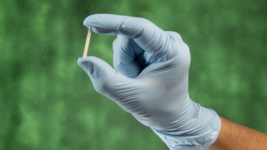 Mão com luva médica segura um implante subdérmico contraceptivo Implanon, método de longa duração utilizado para prevenção da gravidez.