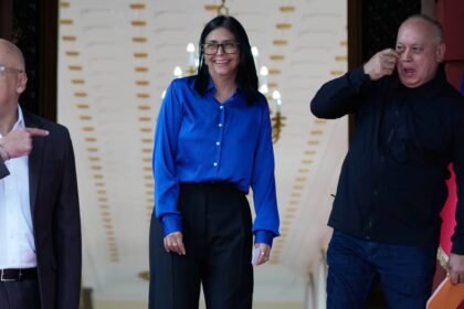 Delcy Rodríguez sorri entre Diosdado Cabello e Jorge Rodríguez no Palácio de Miraflores, em Caracas, antes de um pronunciamento oficial.