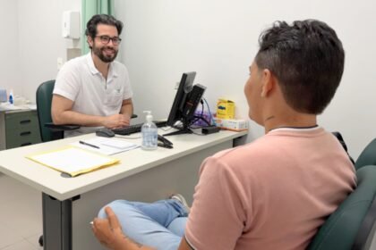 Profissional de saúde conversa com paciente trans em consultório do Hospital Universitário do Ceará, durante atendimento do Sertrans, em ambiente clínico acolhedor.