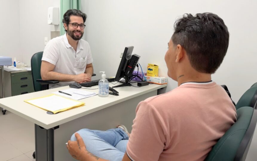 Profissional de saúde conversa com paciente trans em consultório do Hospital Universitário do Ceará, durante atendimento do Sertrans, em ambiente clínico acolhedor.