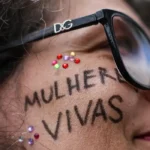 Manifestante durante ato em Brasília contra o feminicídio e a violência contra mulheres, com a mensagem “Mulheres Vivas” escrita no rosto.