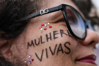 Manifestante durante ato em Brasília contra o feminicídio e a violência contra mulheres, com a mensagem “Mulheres Vivas” escrita no rosto.