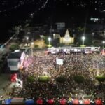 Vista aérea da Praça de São Francisco tomada por milhares de foliões durante o Carnaval 2026 de Cascavel, à noite, com palco iluminado e estrutura de evento.