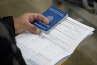 Pessoa segurando Carteira de Trabalho e Previdência Social sobre documentos, simbolizando geração de emprego no Ceará.