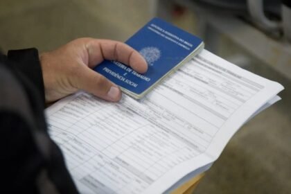 Pessoa segurando Carteira de Trabalho e Previdência Social sobre documentos, simbolizando geração de emprego no Ceará.