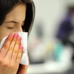 Mulher com sintomas de gripe assoa o nariz com lenço, ilustrando aumento de casos de síndrome gripal em Fortaleza.