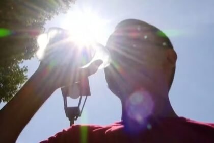 Pessoa se hidrata sob sol forte durante período de calor intenso.