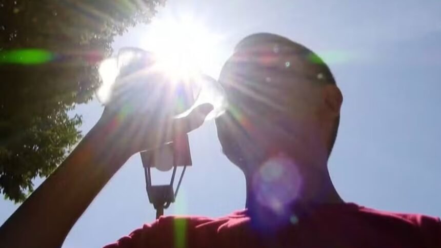 Pessoa se hidrata sob sol forte durante período de calor intenso.