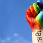 Punho com as cores do arco-íris simboliza a luta contra a violência e a proteção dos direitos da população LGBTI+.